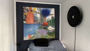 A bedroom with a bed, a painting on the wall, and a black circular object.