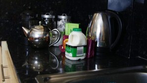 Un plan de travail de cuisine avec une bouilloire, un carton de lait et une boîte verte.