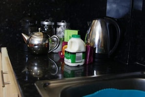 Una encimera de cocina con un hervidor, un cartón de leche y una caja verde.