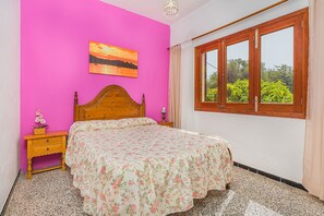 Une chambre avec un lit en bois, un mur rose, une fenêtre donnant sur un paysage verdoyant et un tableau au-dessus du lit.