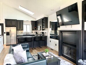 A modern kitchen with dark cabinetry, a stainless steel refrigerator, and a central island with bar stools. - Modern 3 bd next to playground, trials and park (Westerville)