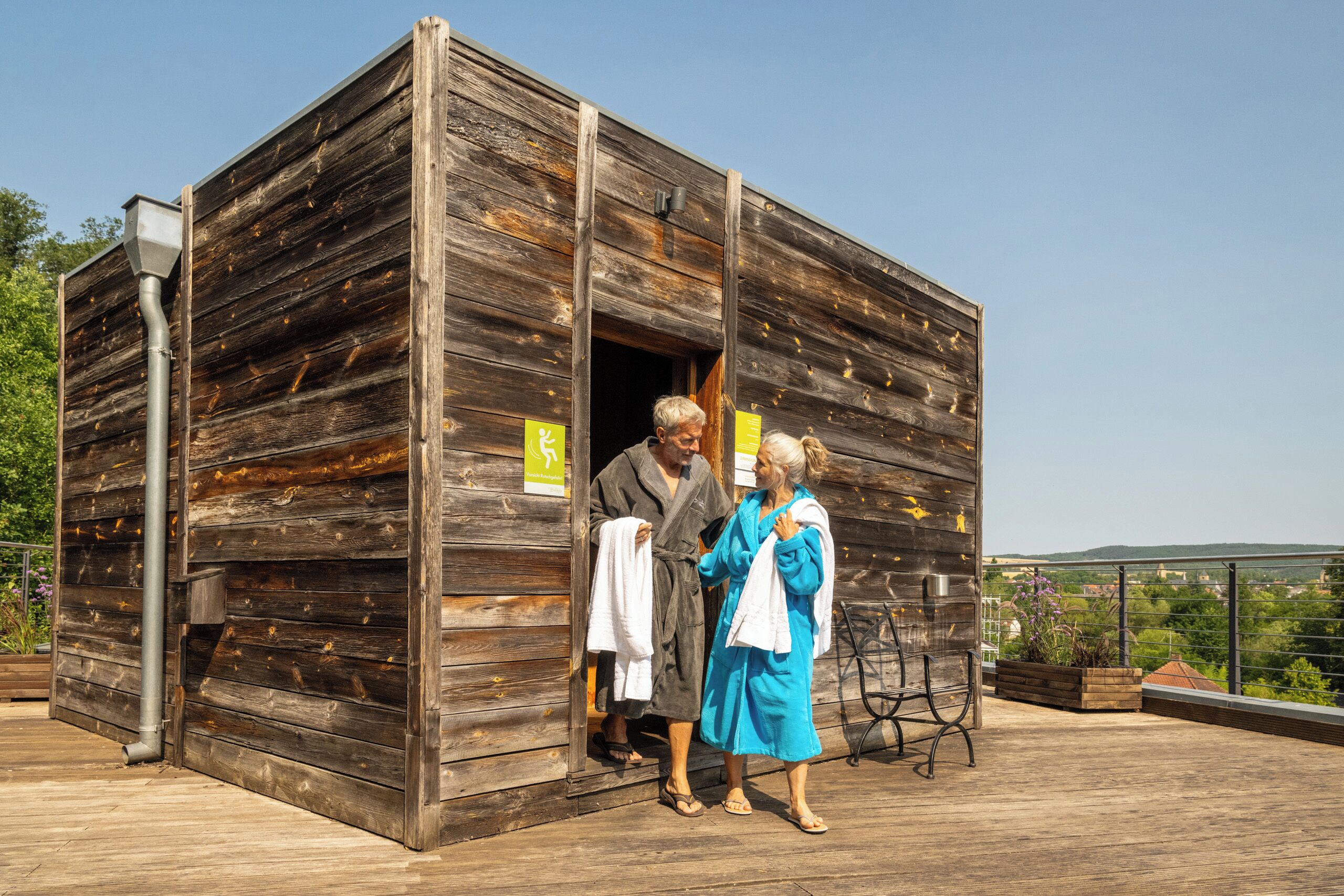 A rustic wooden cabin with a metal door, a small outdoor seating area, and a view of the surrounding landscape.