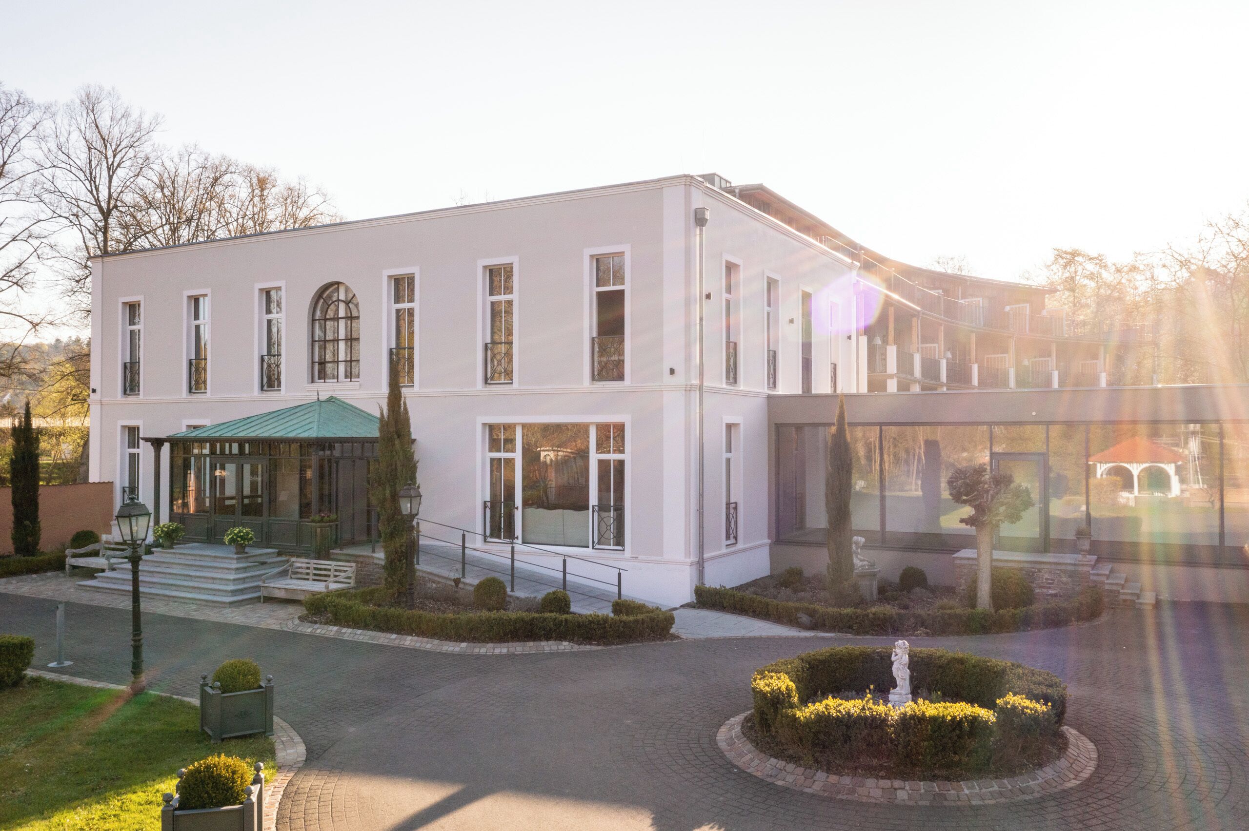 A modern building with a white facade, large windows, and a covered entrance.