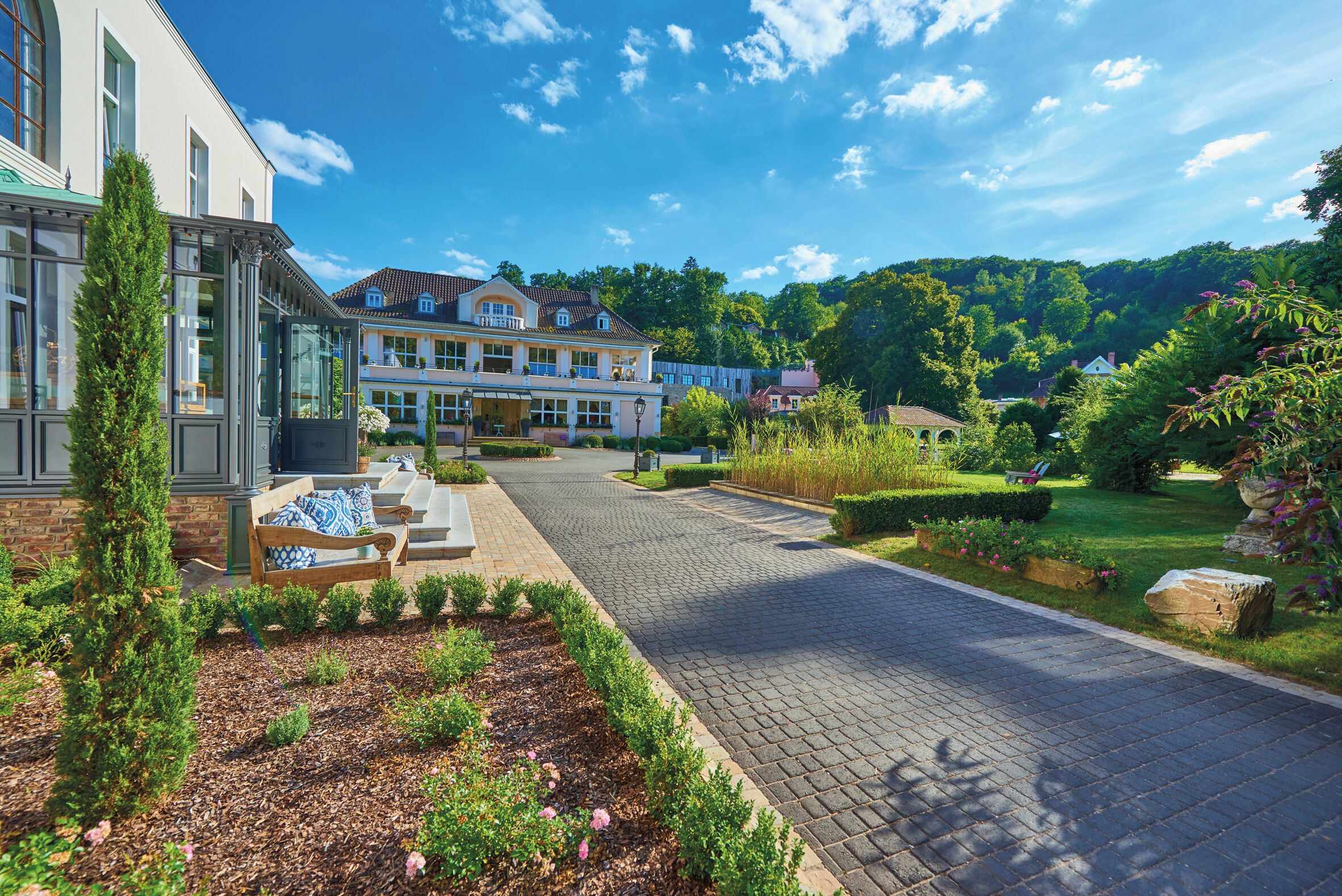A spacious courtyard with a paved walkway, a bench, and a well-maintained garden with various plants and flowers.