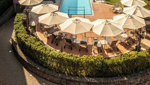 Una piscina con sillones y sombrillas, rodeada de un jardín ajardinado y un camino de ladrillo.