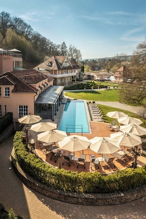 Piscina com espreguiçadeiras e guarda-sóis, cercada por um jardim ajardinado e um caminho de tijolos.