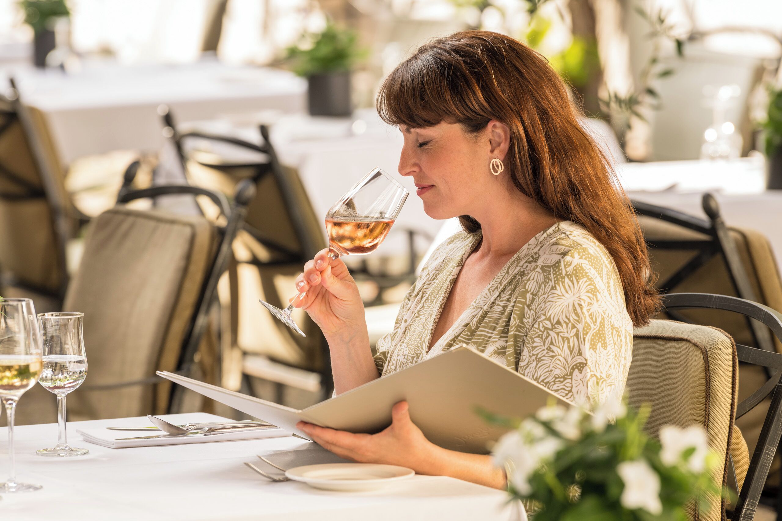 Una donna seduta a un tavolo con un bicchiere di vino, un tablet e un quaderno.