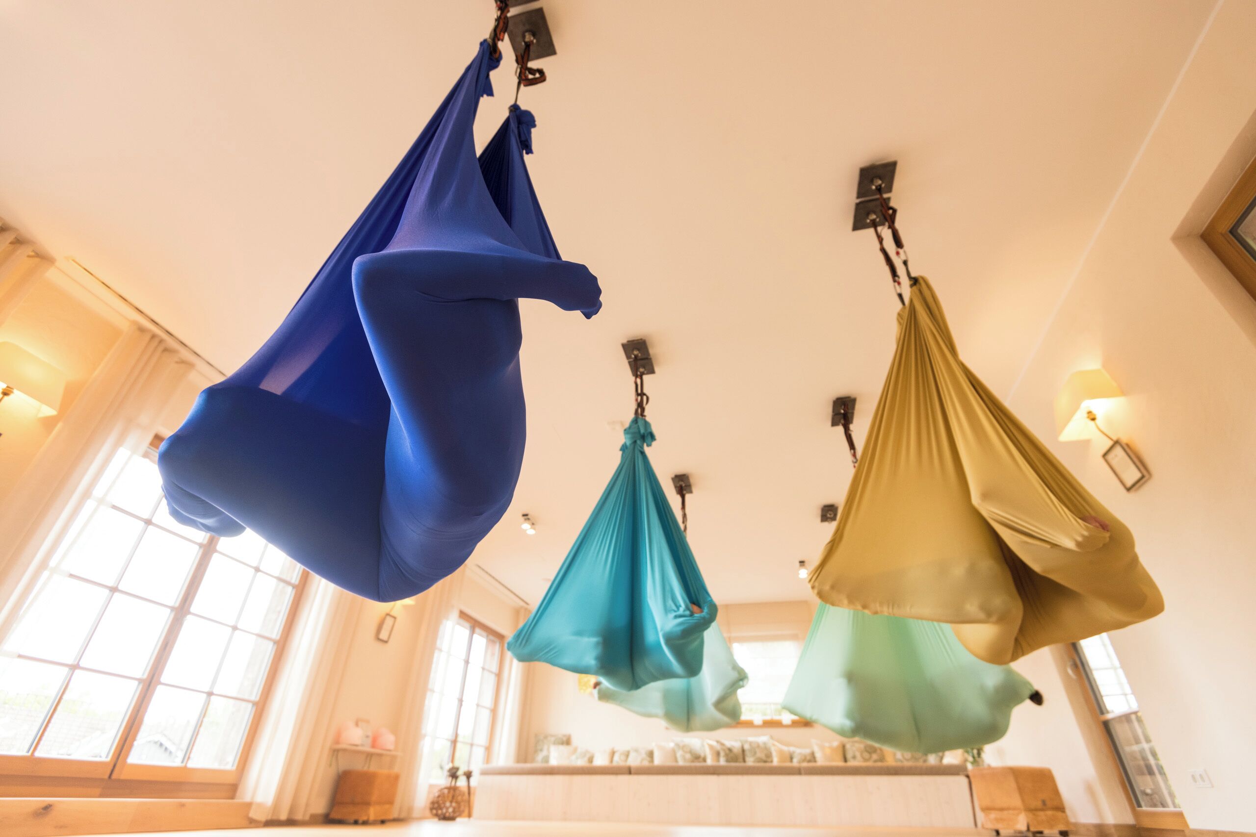 A room with three suspended hammocks in blue, teal, and gold.