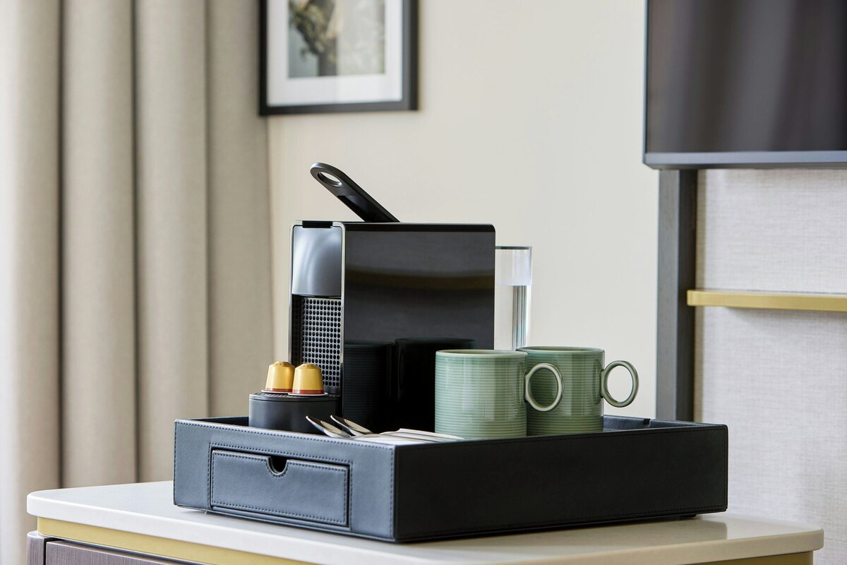 A compact kitchen setup with a coffee maker, a mug, and a small appliance on a white countertop.
