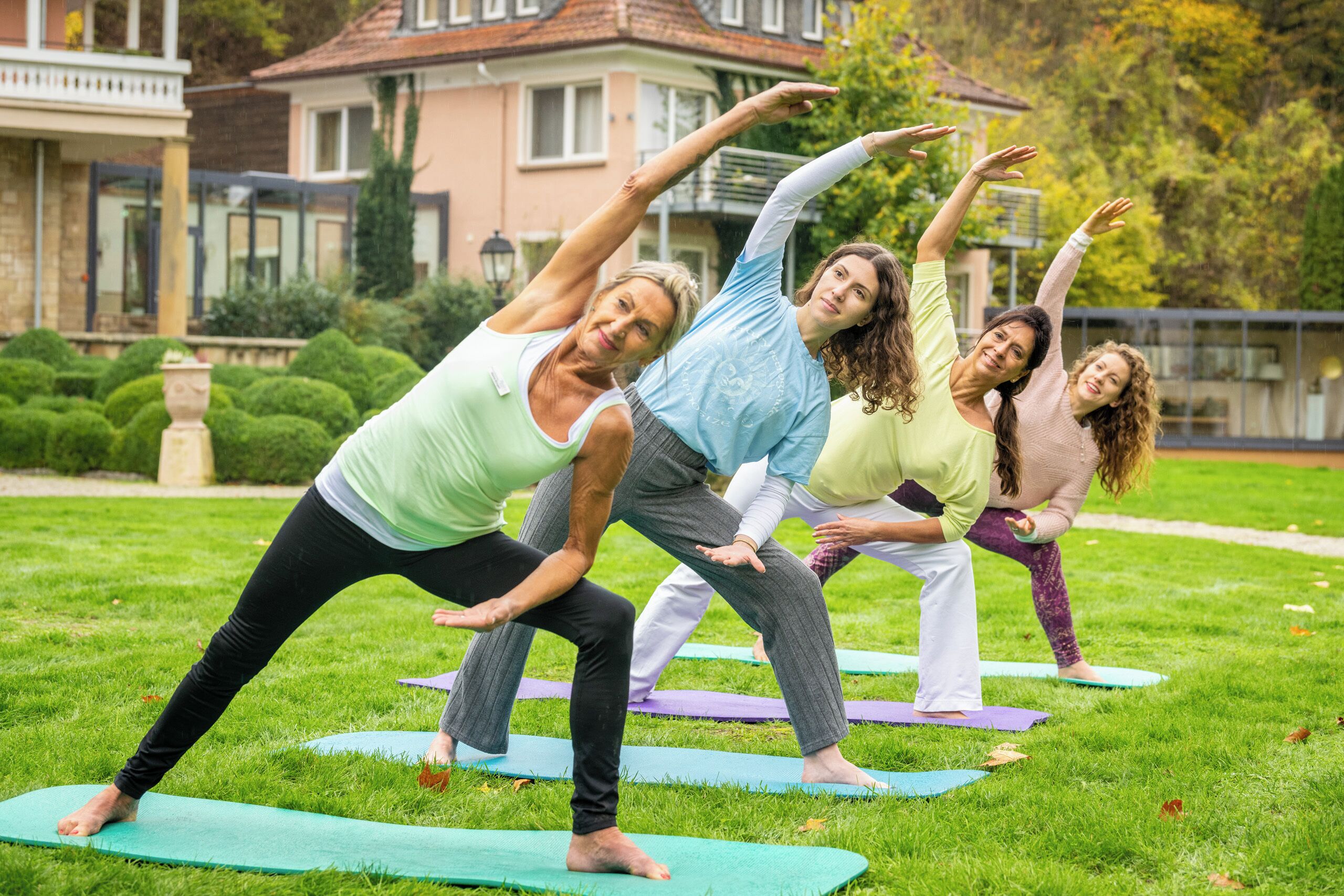 Quatro pessoas praticando yoga em tapetes em uma área gramada, com casas ao fundo.