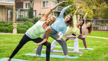Quatro pessoas praticando yoga em tapetes em uma área gramada, com casas ao fundo.