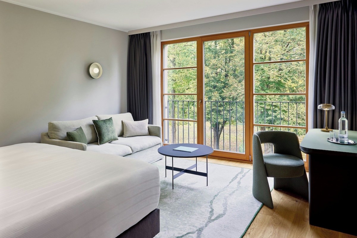 A hotel room with a bed, a sofa, a round table, a chair, and a desk.