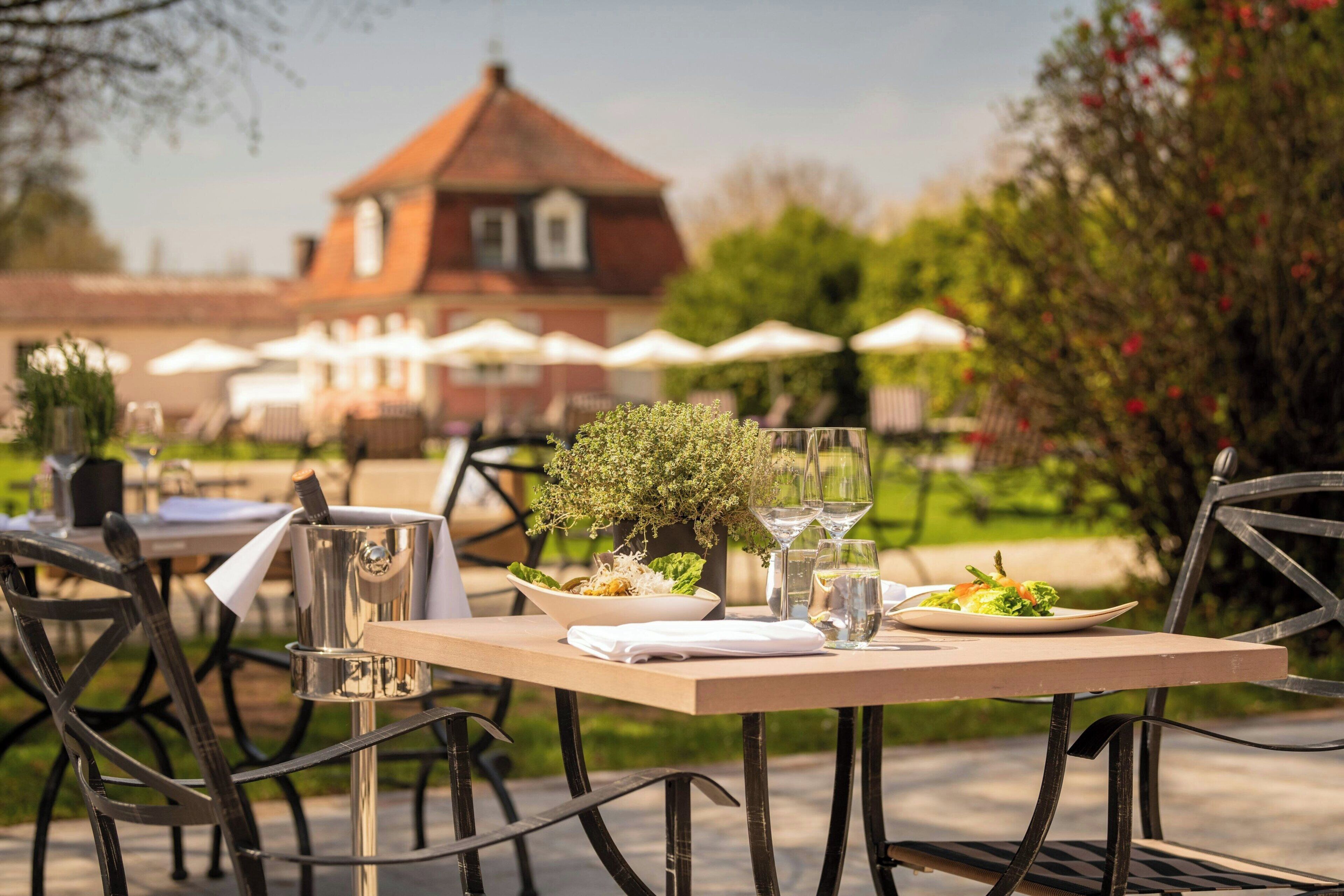 An outdoor dining area with tables, chairs, and umbrellas. There is a building with a red roof in the background.