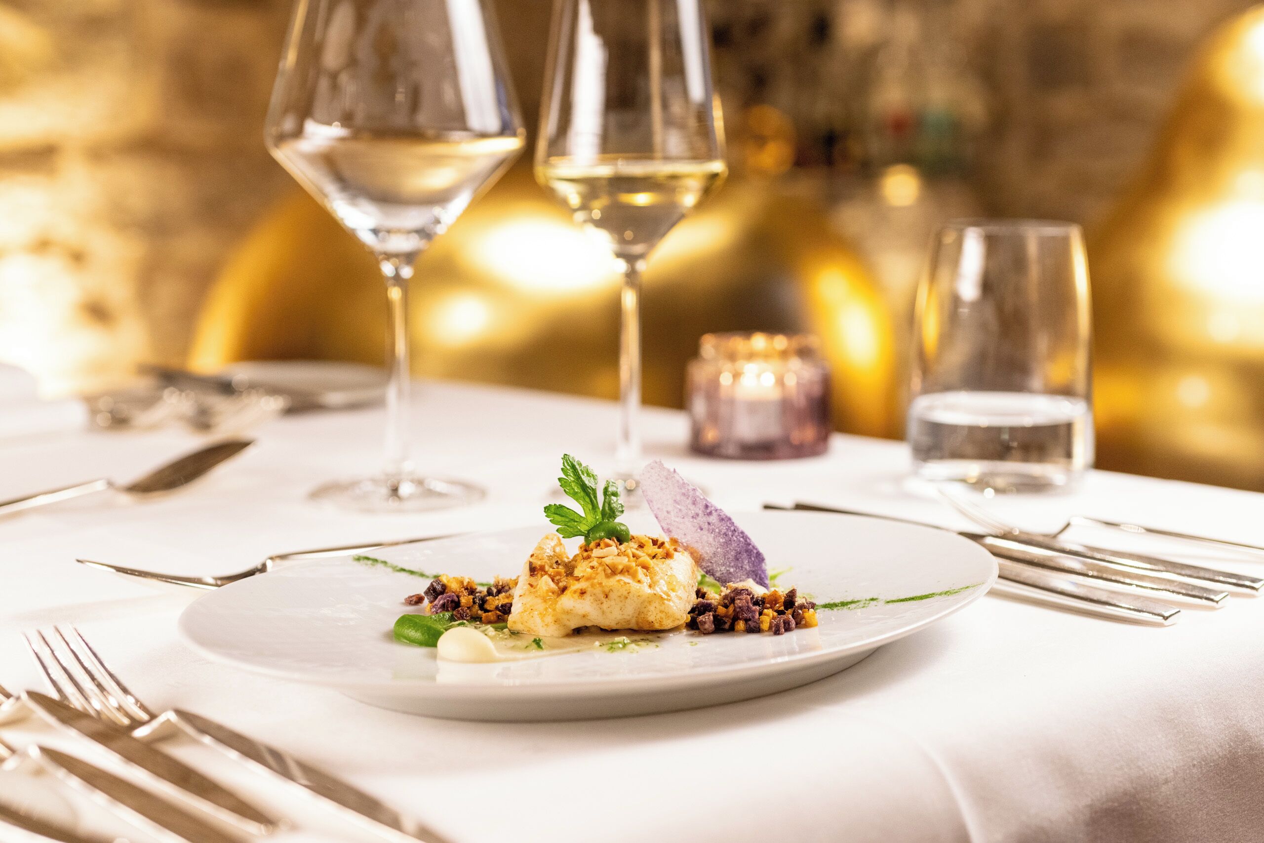A formal dining setting with a white tablecloth, a plate of food, and wine glasses.