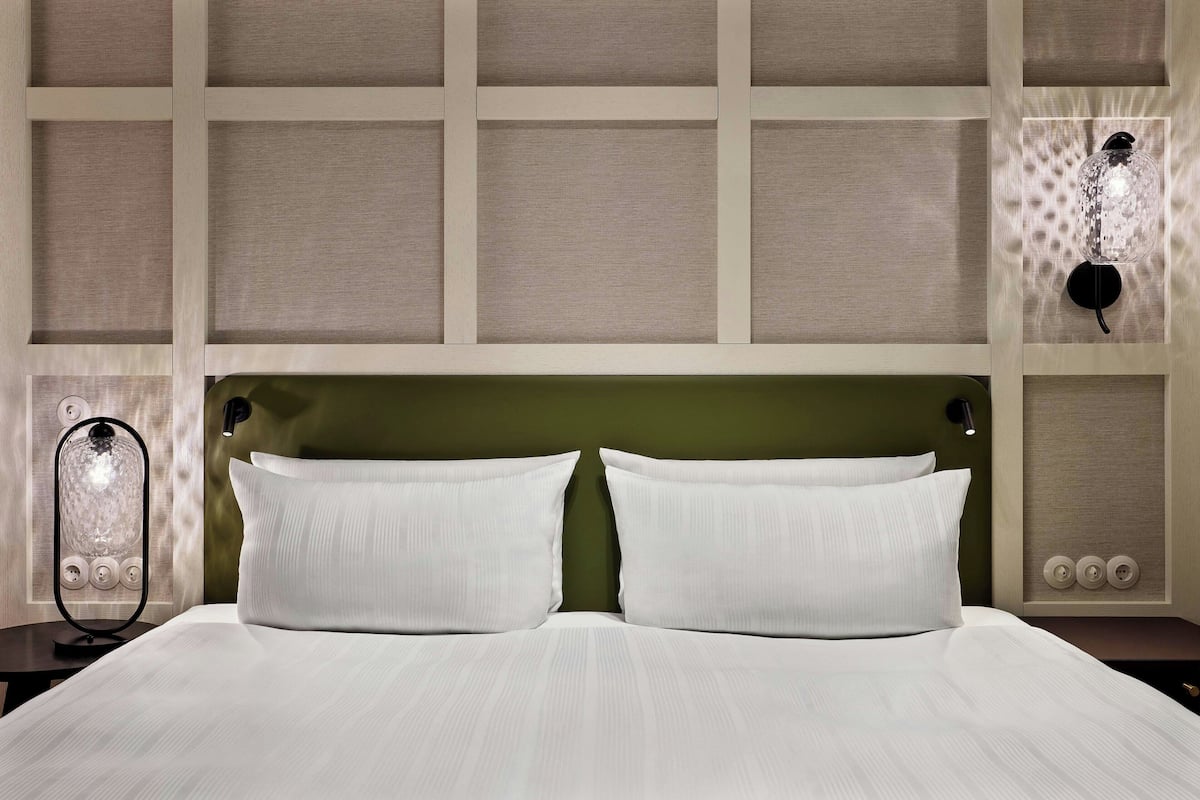 Cama bem arrumada com duas almofadas, cabeceira e luminária fixada na parede.