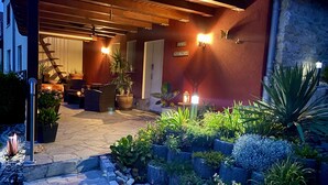 Un espace extérieur bien éclairé, avec un patio, un sol en pierre, des plantes en pot et un mur en pierre.