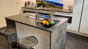 Une cuisine moderne dotée d’un îlot central, d’une grande fenêtre offrant une vue panoramique et de deux chaises en osier.