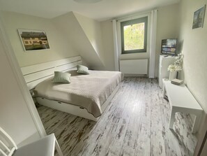 A bedroom with a bed, a bedside table, a radiator, a window, and a picture on the wall.