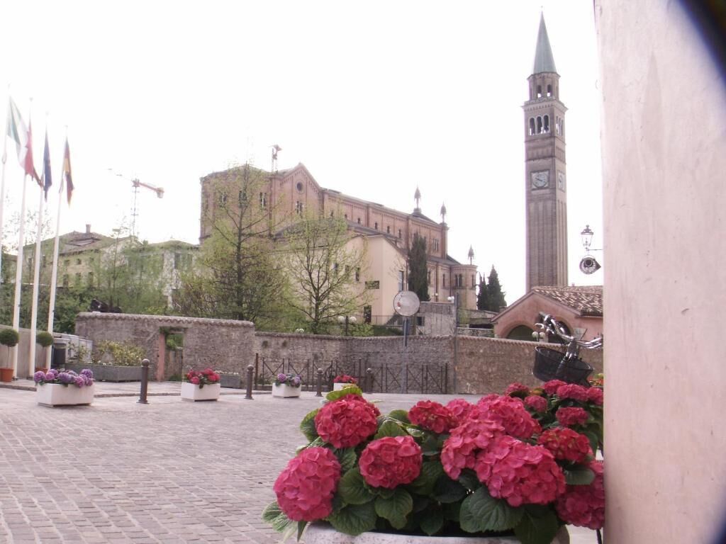 A courtyard with a historic building, a clock tower, and flower beds.
