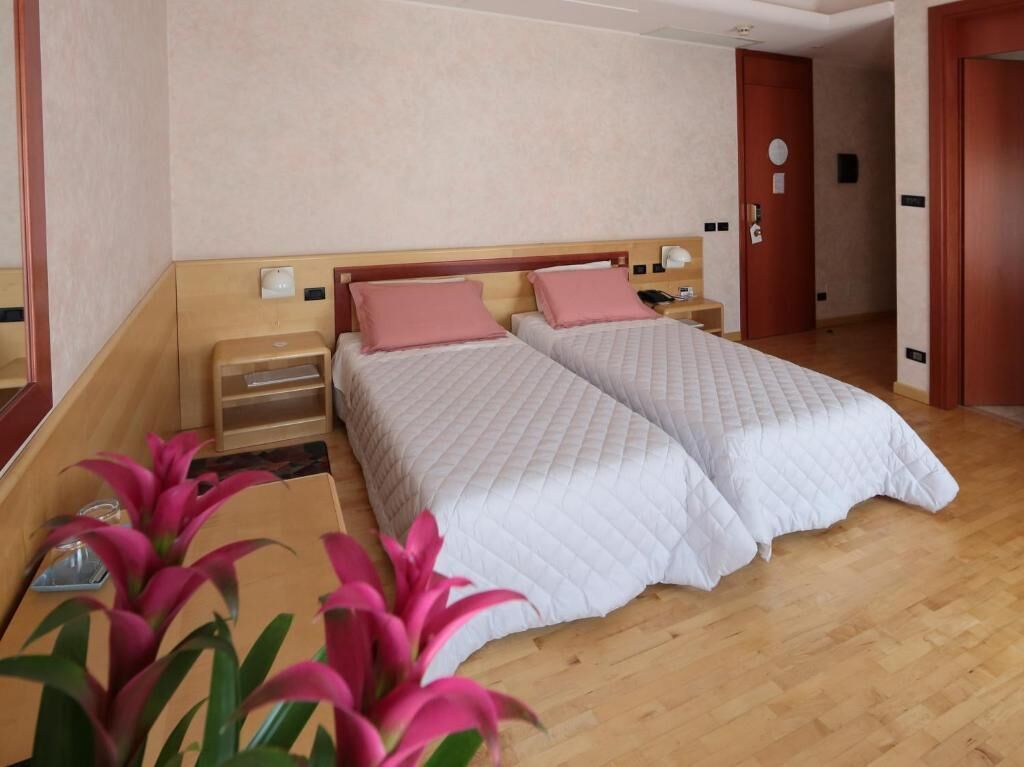 A hotel room with two beds, wooden headboards, bedside tables, and a nightstand with a lamp.