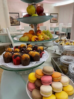 Un bufé con diferentes opciones de comida, incluyendo frutas, pasteles y macarons.