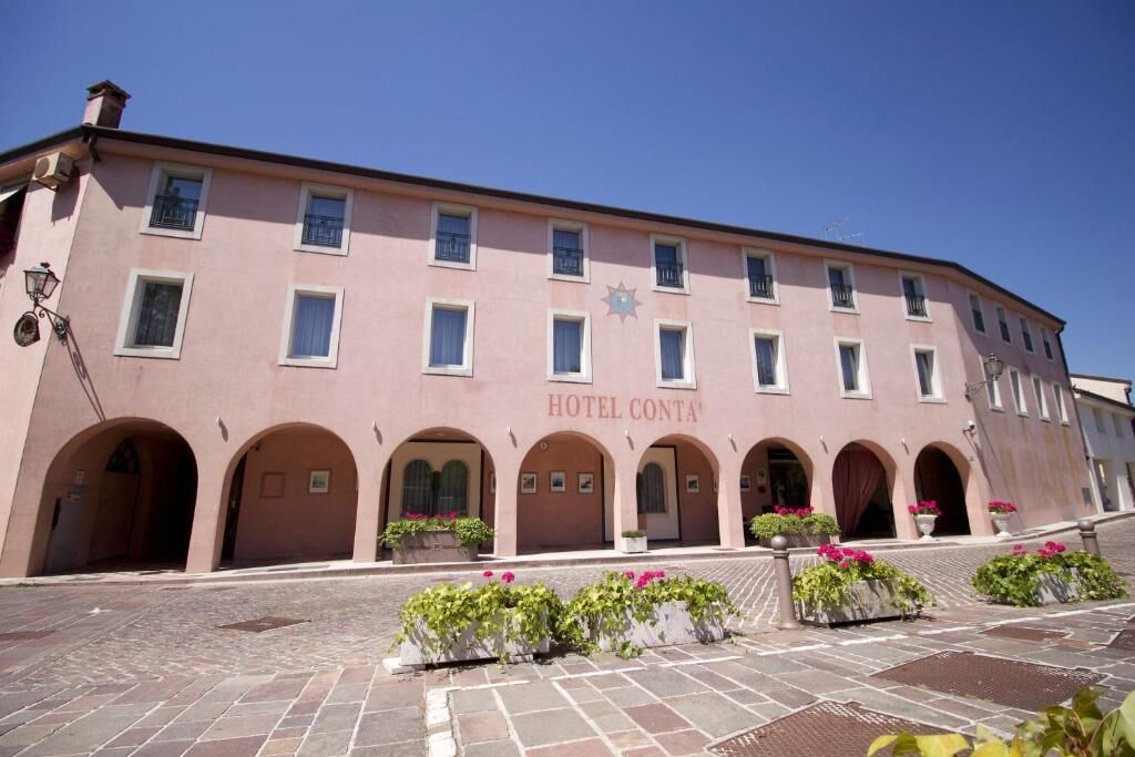 A pink building with the sign "HOTEL CONTA" and arched doorways.