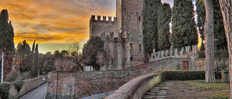 A historic stone castle with a tall tower, surrounded by trees and a stone pathway.