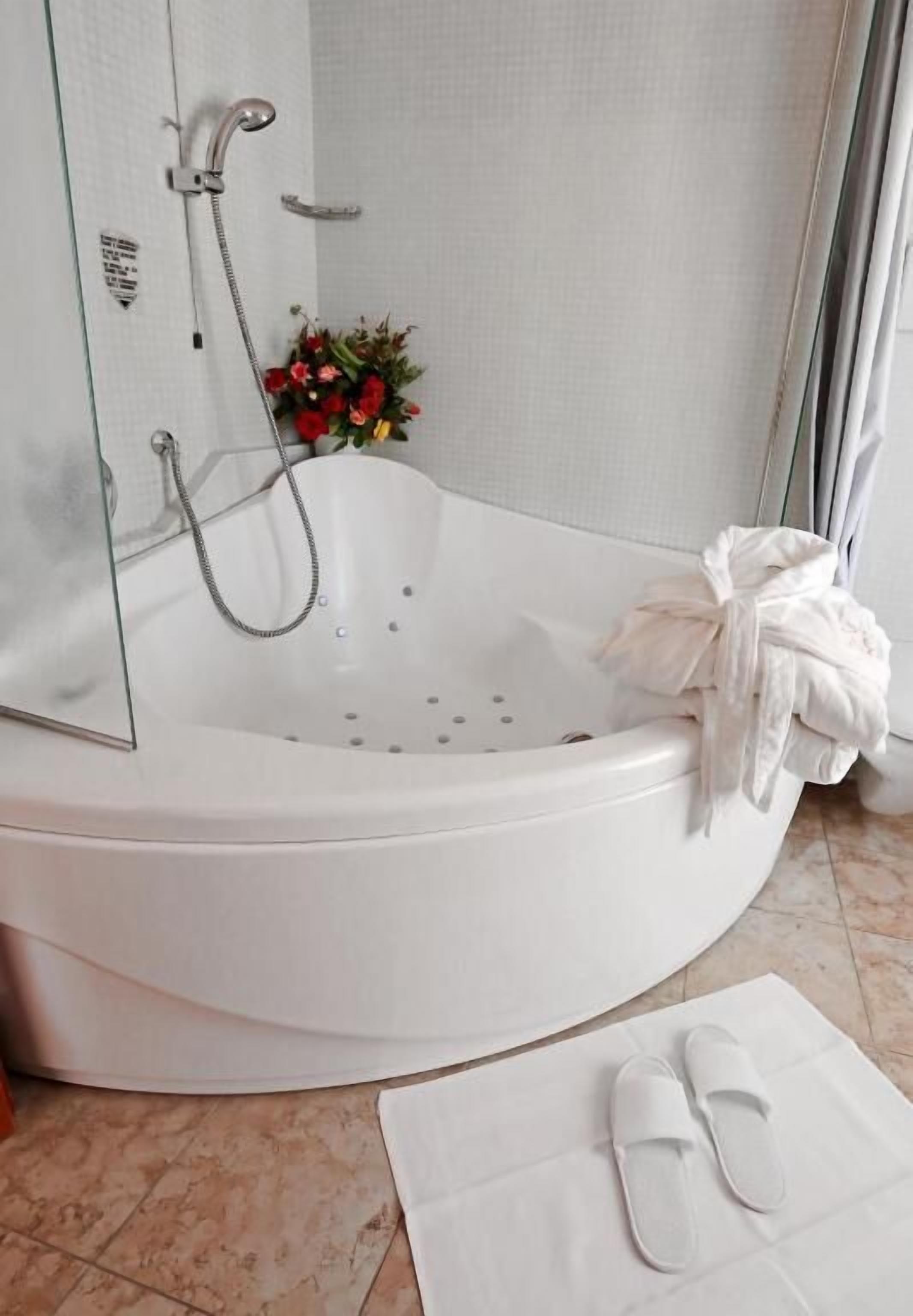 Une salle de bain moderne avec une baignoire aux lignes courbes, une pomme de douche et un petit arrangement floral.