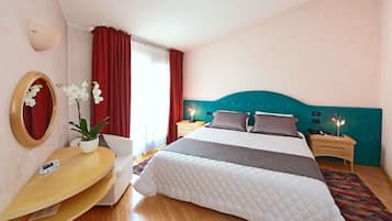 Une chambre d’hôtel comprenant un lit, des tables de chevet, un bureau, une chaise, un miroir et une plante en pot.
