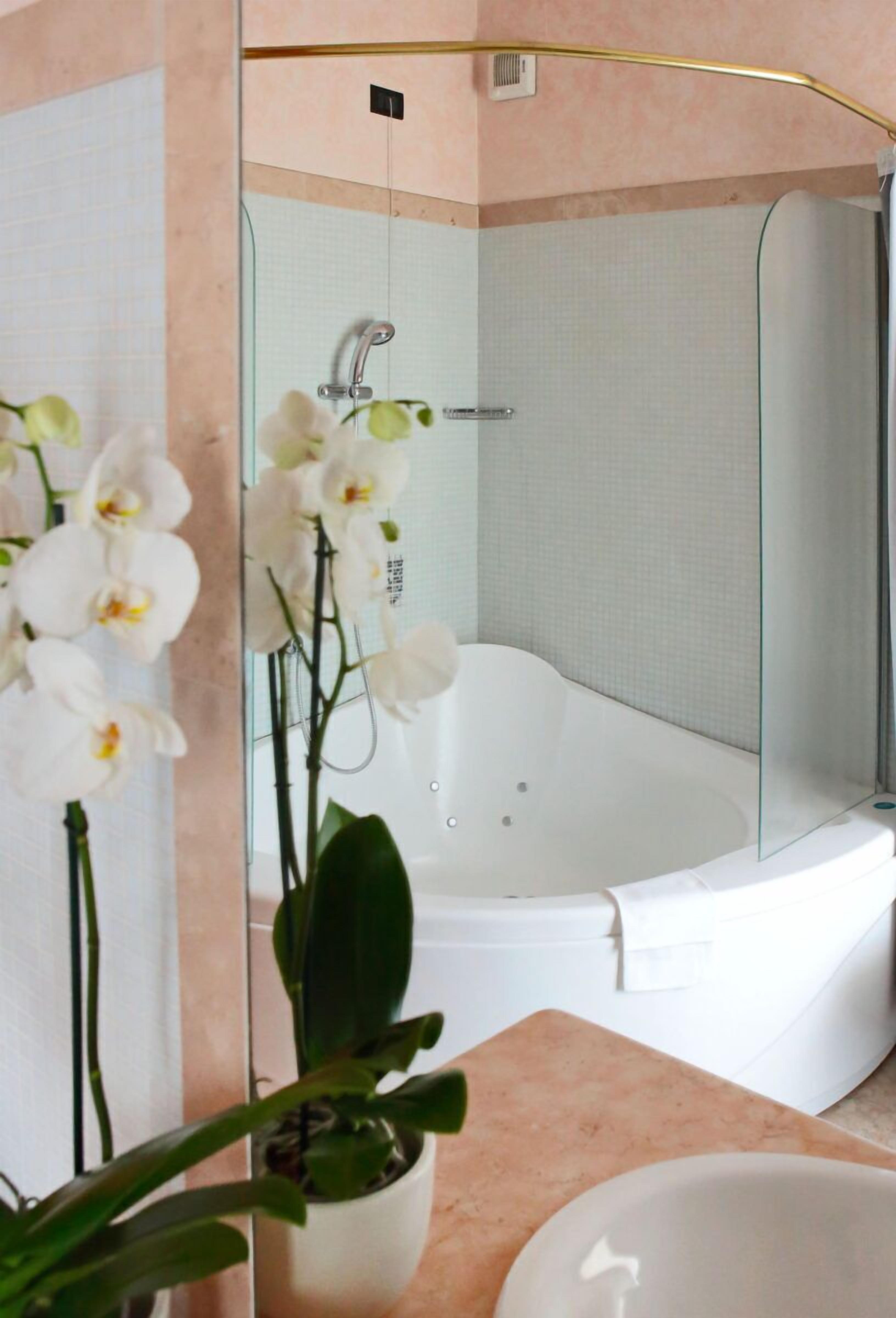 A modern bathroom with a glass-enclosed shower, a white bathtub, and a potted orchid plant.