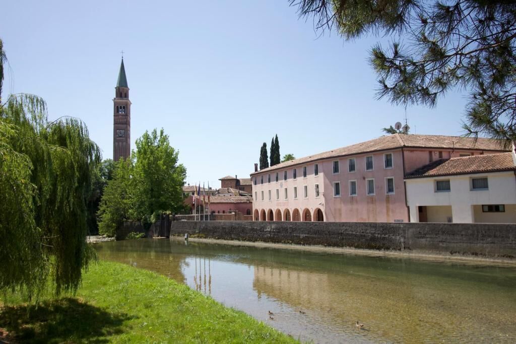 Ein Fluss mit Gebäuden am rechten Ufer, darunter ein Turm im Hintergrund.
