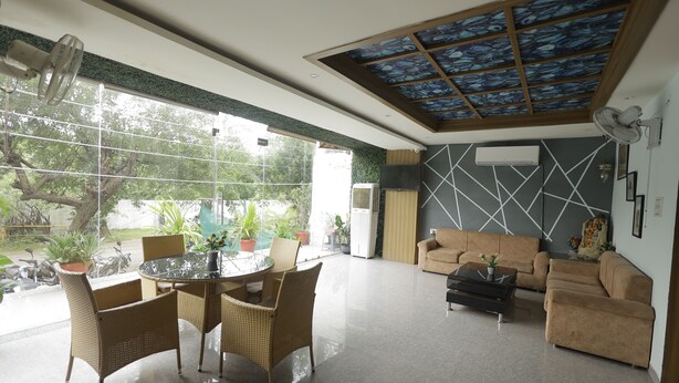A spacious living area with a round glass table, wicker chairs, a sofa, and a ceiling fan. - HOTEL PRIDE INN (Bhopal)
