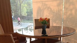 A round glass table with wicker chairs, a vase with flowers, and a view of a street with a cyclist. - HOTEL PRIDE INN (Bhopal)