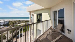 Un balcón con vista a la playa, una silla y una mesa.