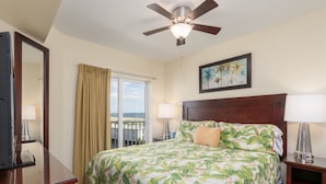 A hotel room with a bed, a ceiling fan, a window with curtains, a painting on the wall, and a nightstand with a lamp. - 607S-Penthouse-Gulf View, Top Floor, 2/2 on Beach (Treasure Island)