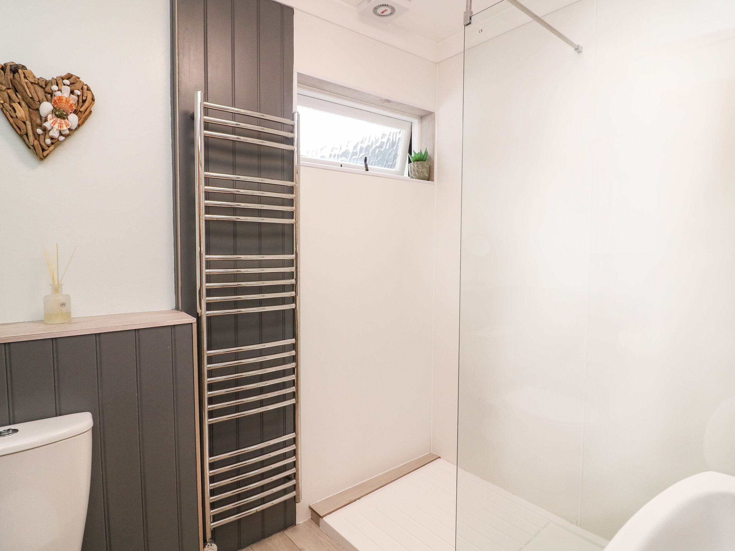 A modern bathroom with a glass shower enclosure, a toilet, and a vanity with a heart-shaped decoration.