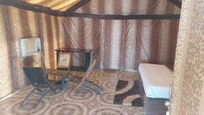 A room with a patterned carpet, a bed, a small table with a picture frame, and a chair. - Shivas Heritage and Sand Dunes (Jaisalmer)