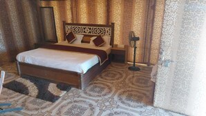 A bedroom with a large bed, a nightstand, a floor lamp, and patterned curtains. - Shivas Heritage and Sand Dunes (Jaisalmer)