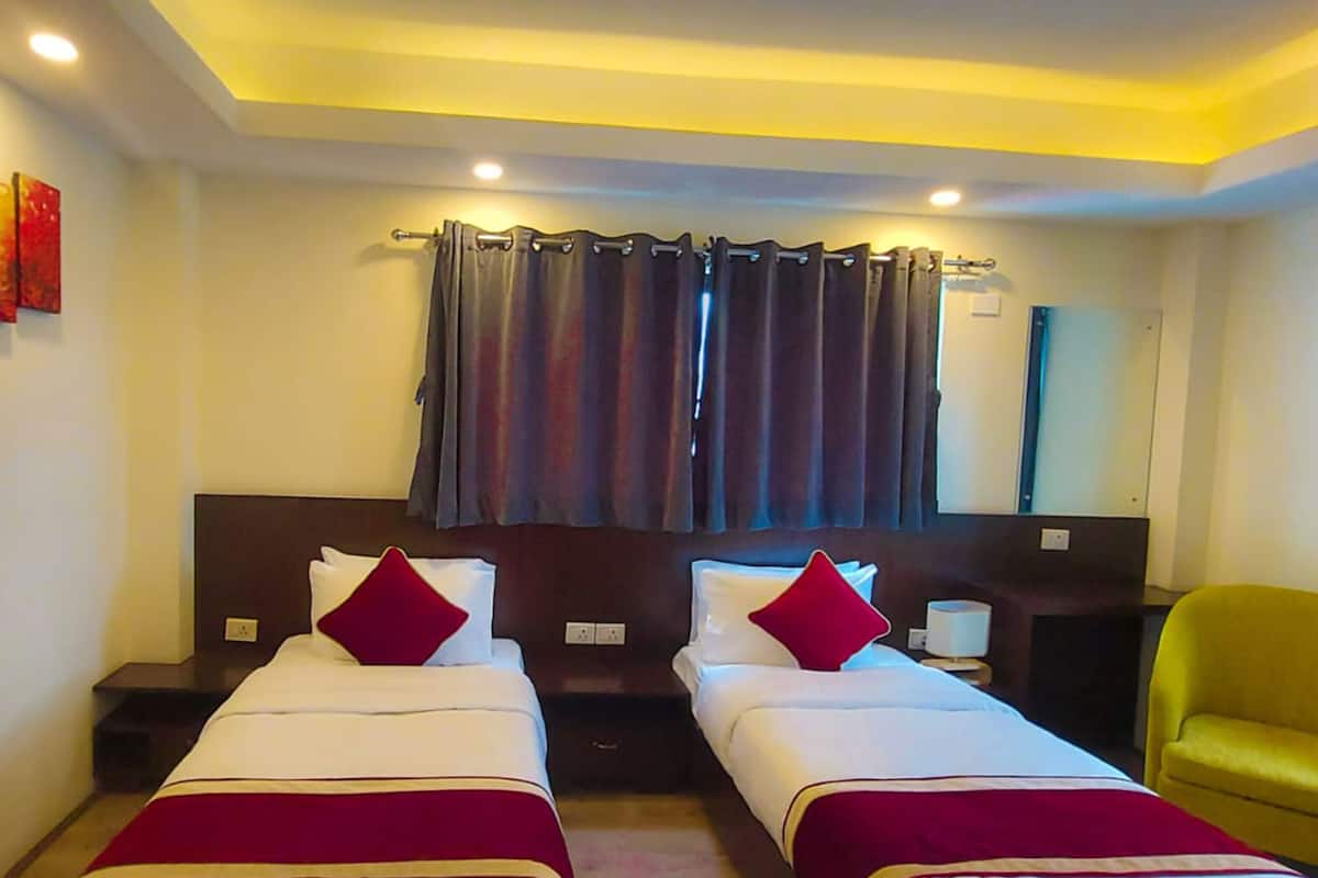 A hotel room with two beds, a nightstand, a chair, and a large window with curtains.
