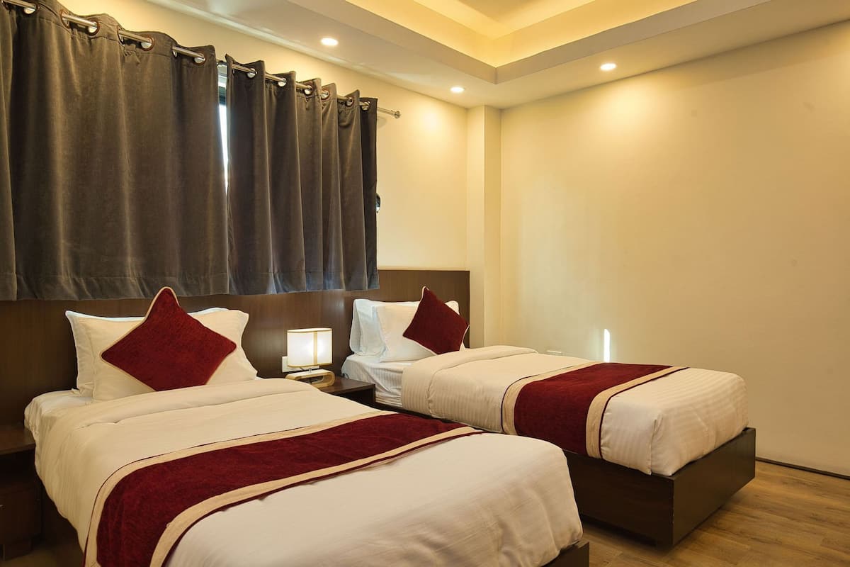 A hotel room with two beds, a nightstand, a lamp, and a window with curtains.