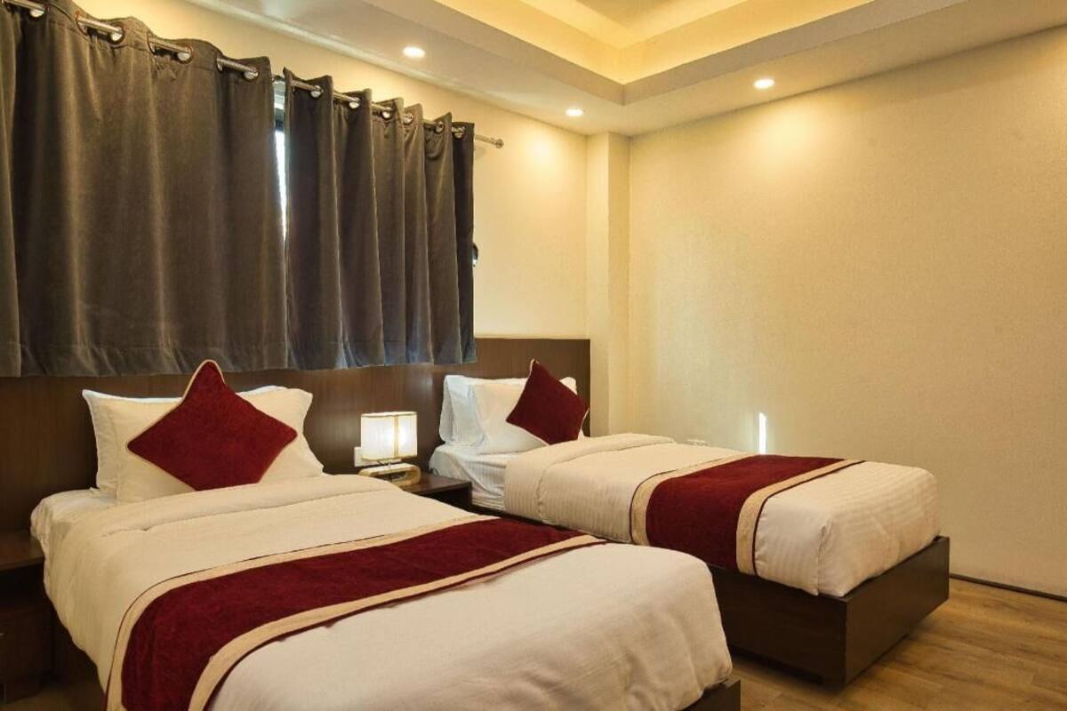 A hotel room with two beds, a headboard, a nightstand, and a window with curtains.
