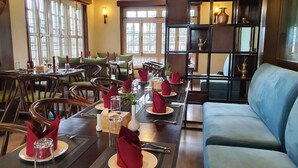 A dining area with tables set for four, wooden chairs, and a blue sofa. - Hotel Grand View (Kathmandu)