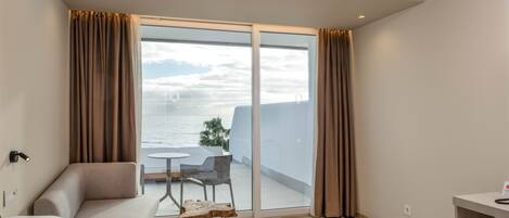 Habitación de hotel moderna con una cama grande, una mesita y una silla. Tiene un balcón con vistas al mar.