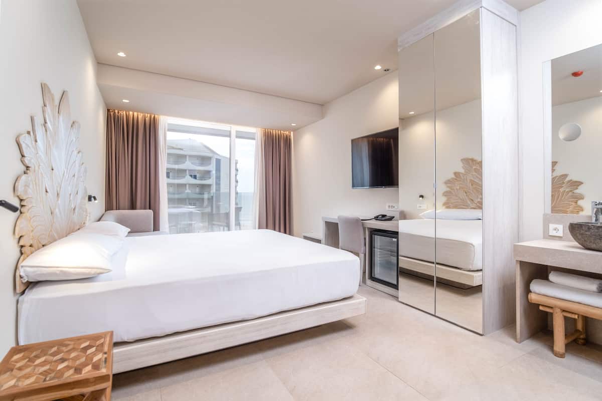 A modern hotel room with a large bed, a desk, a TV, and a mirror.