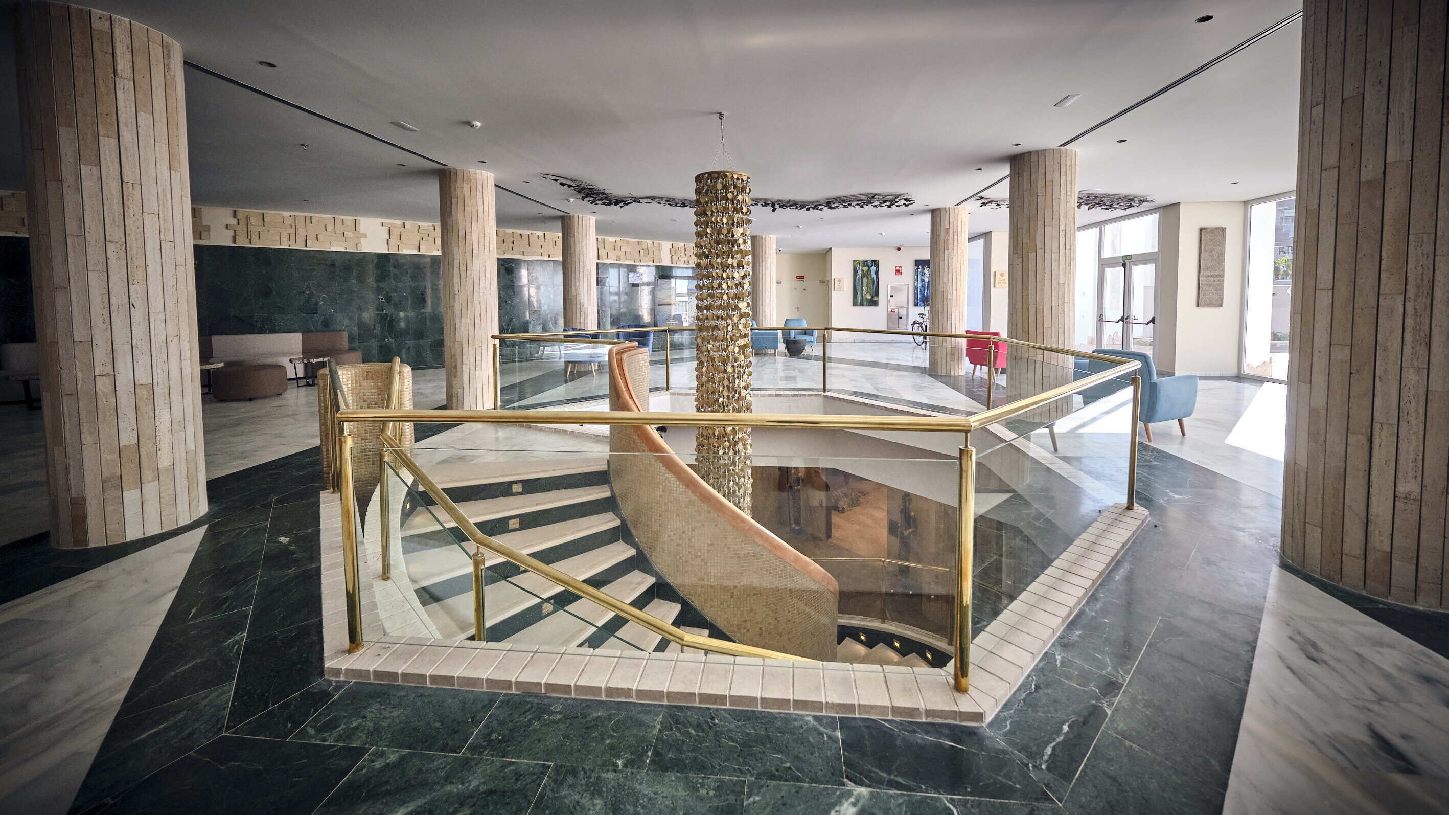 A spacious lobby with a glass-walled staircase, marble flooring, and modern furnishings.