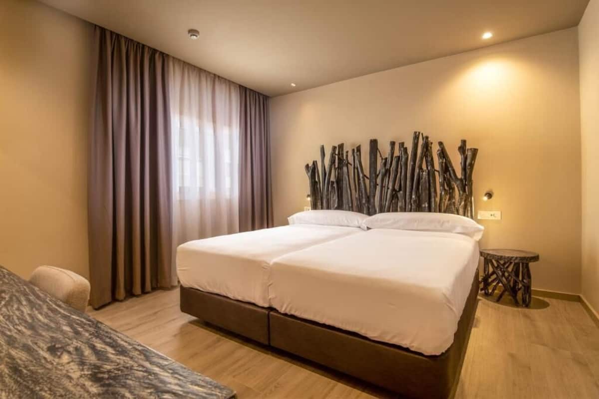 A modern hotel room with a large bed, a side table, and a decorative wall piece.