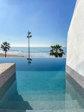 A clear view of a swimming pool with a view of the ocean, a street lamp, and palm trees. - Hotel Cádiz Bahía by Q Hotels (Cádiz)