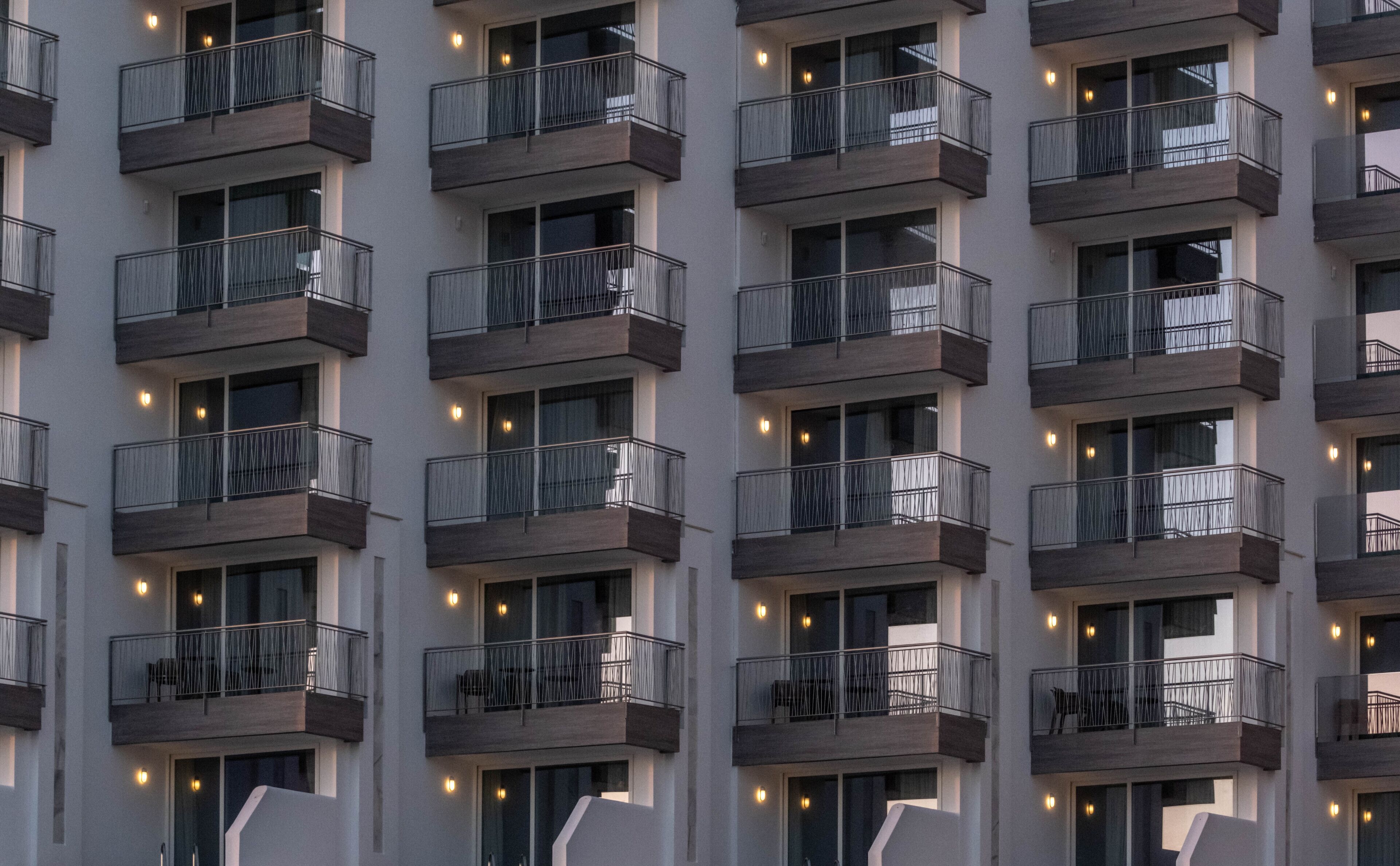 A modern building with multiple balconies, each with a metal railing and a small table.