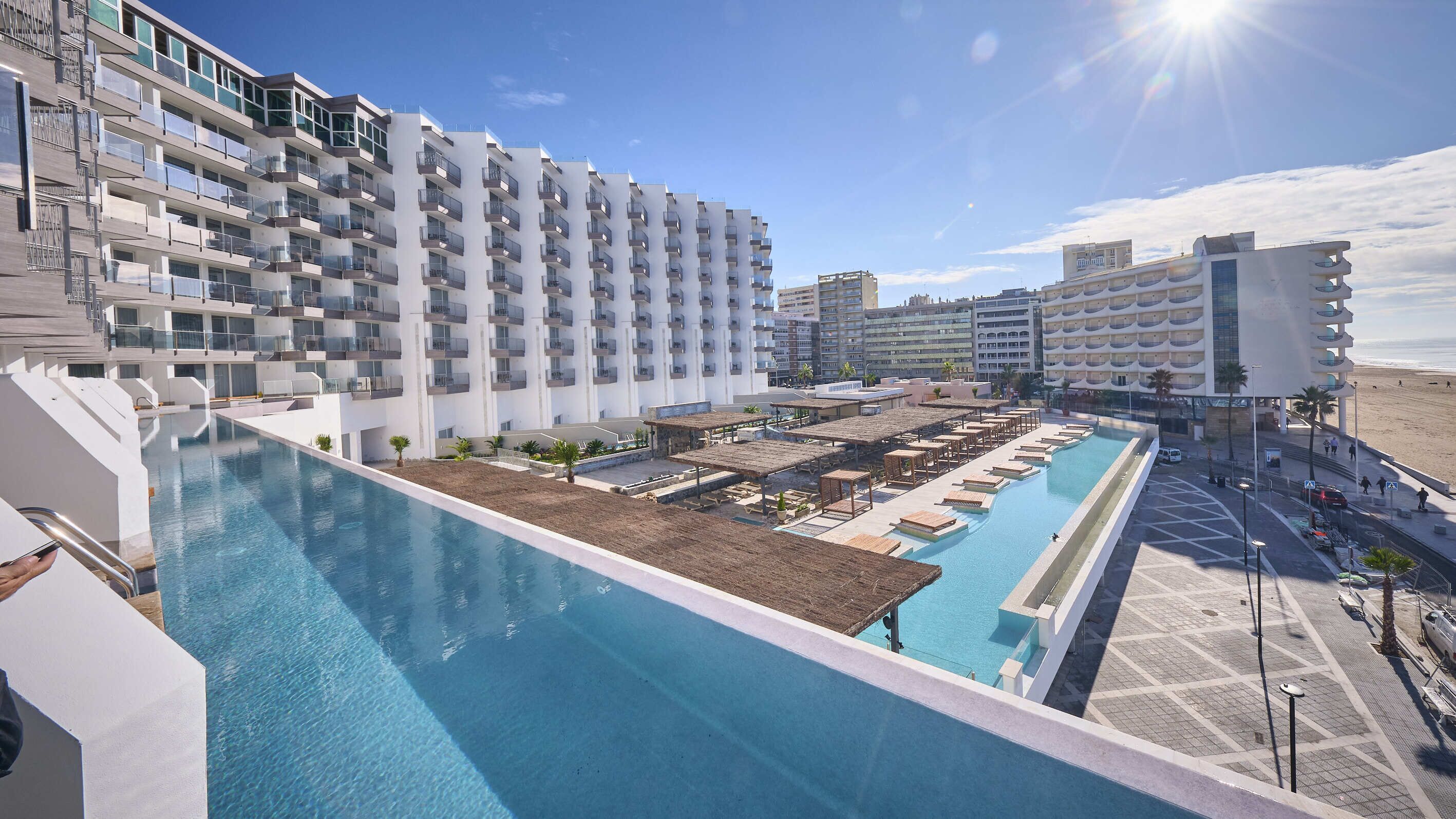 Un hôtel moderne doté d’une grande piscine, de nombreux balcons et offrant une vue sur la plage.
