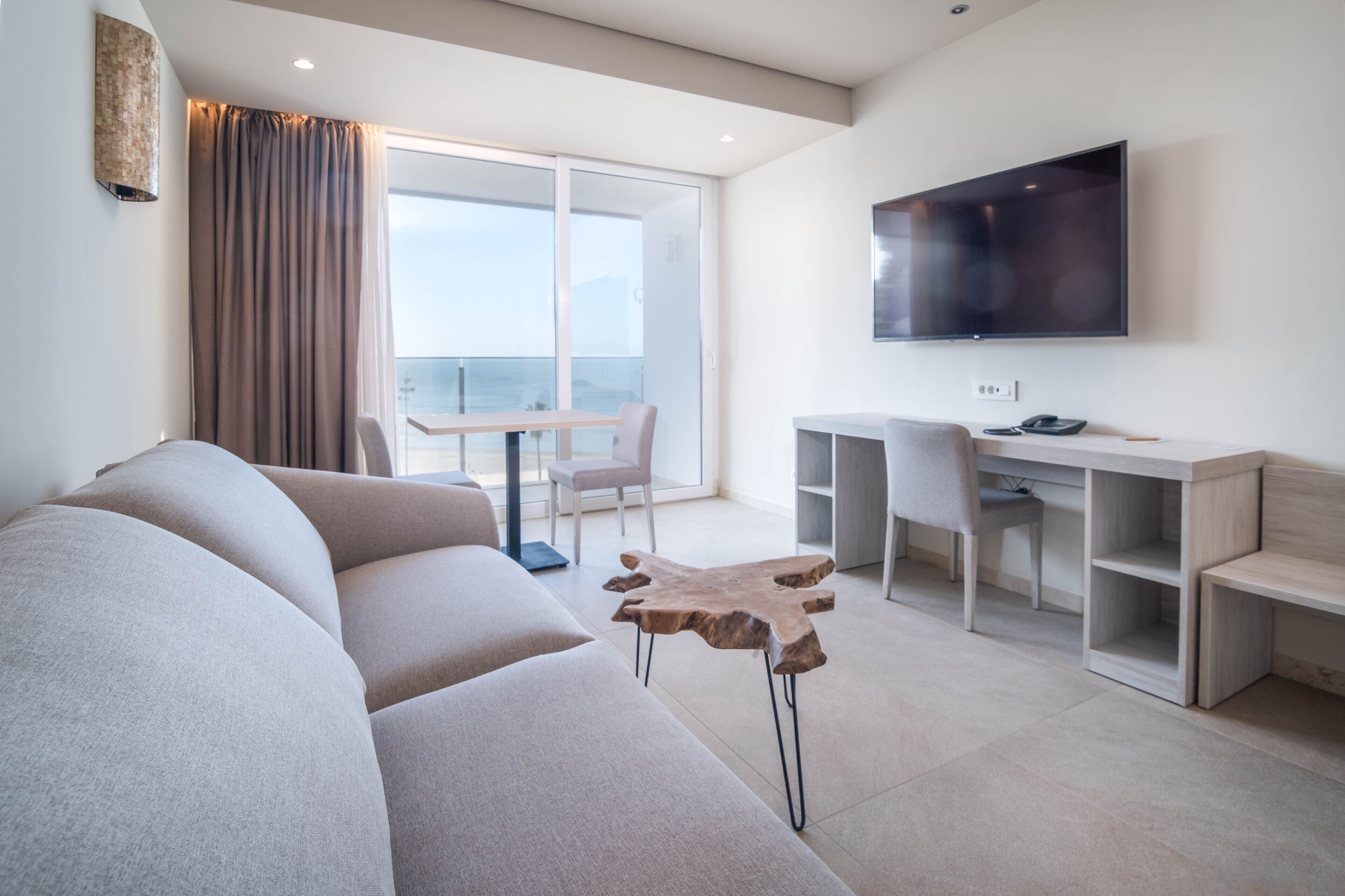 Una sala de estar moderna con un sofá grande, una mesa de centro de madera, un televisor de pantalla plana montado en la pared y un balcón con vistas.
